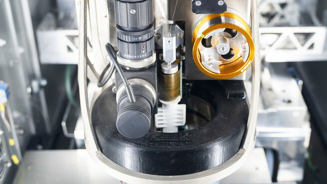 Nahaufnahme einer industriellen Präzisionsmaschine die eine eingespannte, blaue Platine bearbeitet.