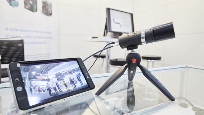 A small camera on a tripod, next to a screen on which the image of the camera is transmitted.
