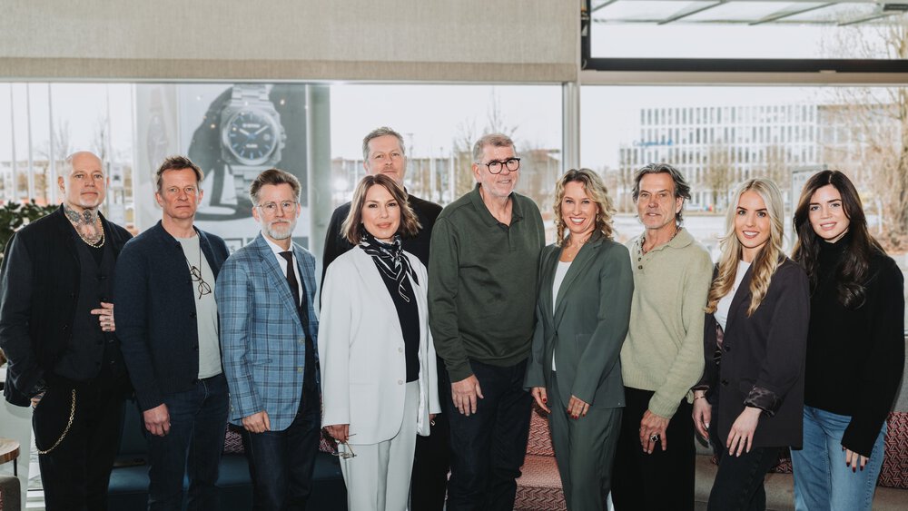 Six men and four women in festive attire pose smiling in front of a large window front for a group photo.