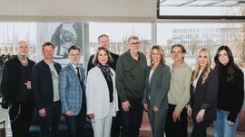 Six men and four women in festive attire pose smiling in front of a large window front for a group photo.
