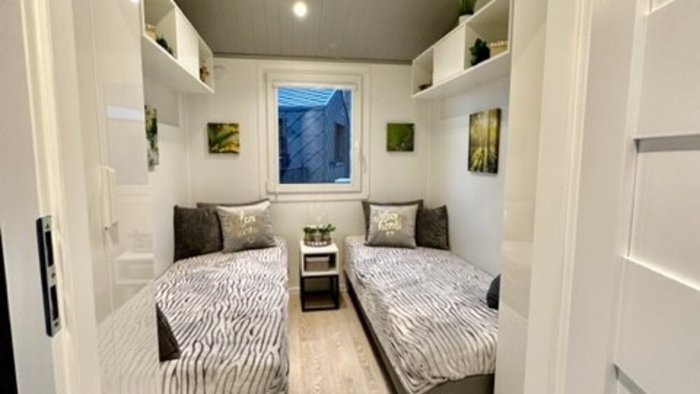 Modernes, gemütliches Zimmer mit zwei Einzelbetten, einem Fenster und minimalistischer Einrichtung auf hellem Holzboden.