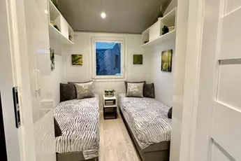 Modernes, gemütliches Zimmer mit zwei Einzelbetten, einem Fenster und minimalistischer Einrichtung auf hellem Holzboden.