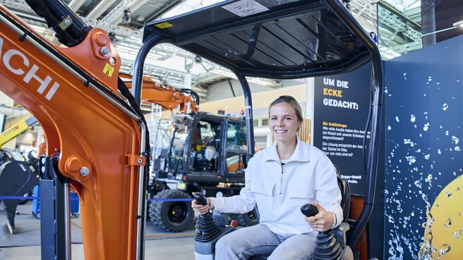 Young woman smiling while sitting in an excavator at a trade fair.