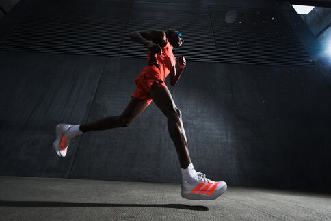 Froschperspektive von der Seite auf einen rennenden Mann mit weiß-orangenen Sportschuhen in orangener Kleidung und mit Sonnenbrille.