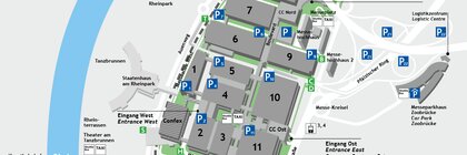 Karte eines Geländeplans der Messe in Köln, mit nummerierten Gebäuden und markierten Parkbereichen in der Nähe eines Flusses und Haltestellen des öffentlichen Nahverkehrs.