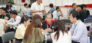 People sitting in groups at a conference, chatting and socializing at tables in a bright room.