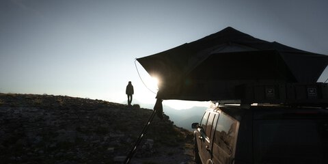 Eine Person genießt den Sonnenuntergang vor einem Dachzelt in den Bergen. Das Bild steht für Freiheit, Natur und Camping mit Dachzelt und passt zur Podcast-Folge über Dachzelte auf der f.re.e.
