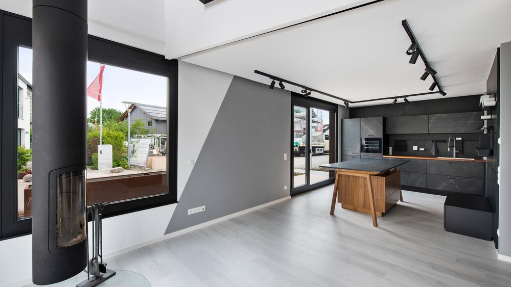 Modernes Wohnzimmer mit großen Fenstern, grauen Wänden, einer schwarzen Küche und einem Stuhl. Helles und geräumiges Interieur.