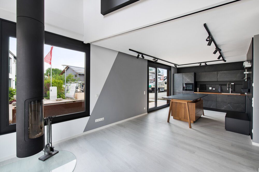 Modernes Wohnzimmer mit großen Fenstern, grauen Wänden, einer schwarzen Küche und einem Stuhl. Helles und geräumiges Interieur.