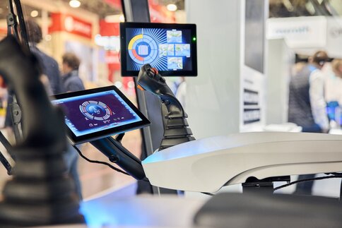 Fahrerkabine mit Joysticks und Displays auf einer Messe ausgestellt.