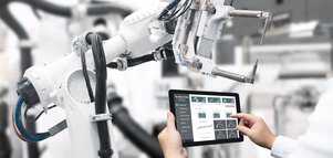 Person controlling a robotic arm in an industrial environment using a tablet.