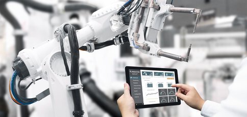 Person, die in einer industriellen Umgebung einen Roboterarm mithilfe eines Tablets steuert.
