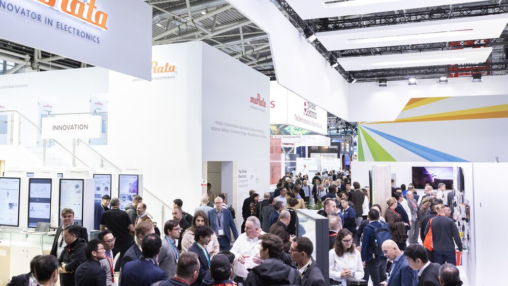 View of an exhibition hall with large, brightly designed exhibition stands and a large number of visitors.