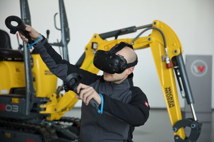 Person nutzt VR-Headset und Controller neben Baumaschinen.