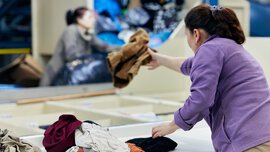 Eine Frau sortiert gebrauchte Kleidungsstücke an einer Textilrecycling-Anlage.
