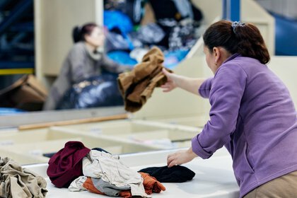 Eine Freu sortiert gebrauchte Kleidungsstücke an einer Textilrecycling-Anlage.