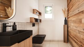 Modernes Badezimmer mit Holzakzenten, schwarzen Armaturen, einer wandmontierten Toilette und einem kleinen Fenster, das Tageslicht hereinlässt.