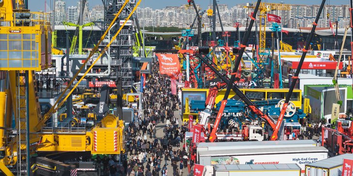 A large crowd is strolling past cranes, lorries and construction machinery at an outdoor trade fair.
