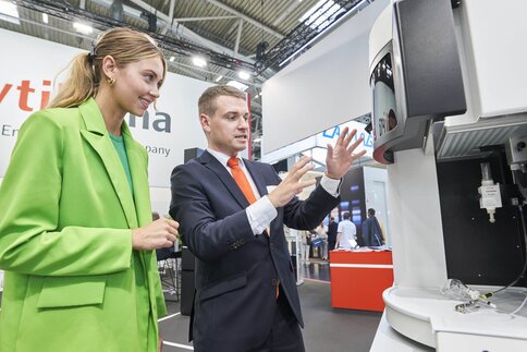 A businessman explains an analytics device to a businesswoman at the exhibitor stand at the analytica trade fair