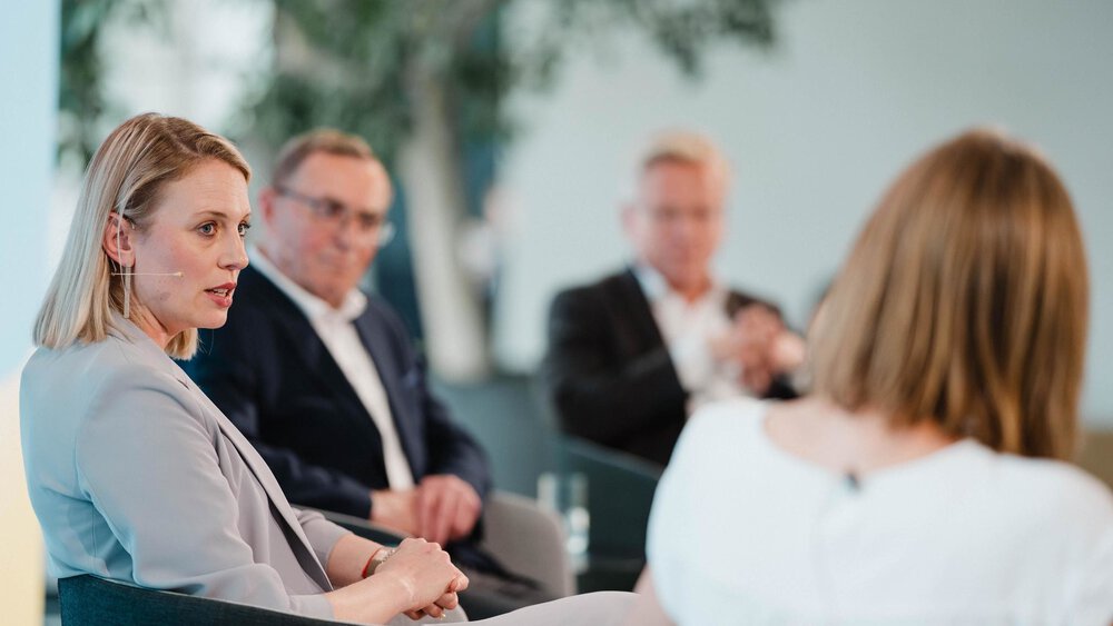 Dr. Lisa Irwin-Broß spricht während der Paneldiskussion auf der Bühne. Im Hintergrund sind weitere Panelteilnehmende und die Moderatorin unscharf zu sehen.