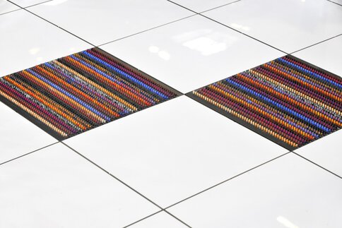 Two colorful woven mats on a shiny white tile floor with a grid pattern.