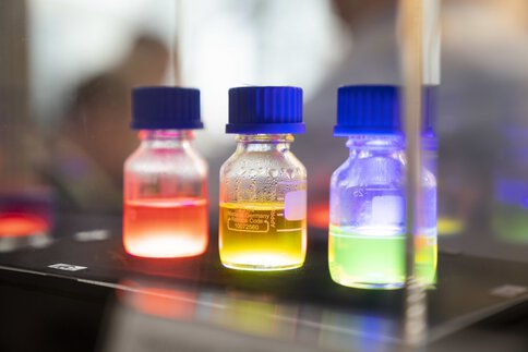 Small glass bottles with brightly colored liquids and blue caps on a dark background.