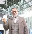 Man in a brown suit holding a ticket in front of the entrance to the Messe München Trade Fair Centre.