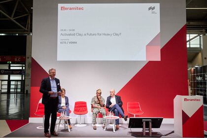 A panel discussion on the trade fair stage on the topic “Activated Clay, a Future for Heavy Clay?” featuring several experts and a moderator.