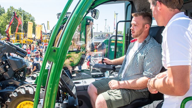 A man in a chequered shirt tests a green tractor on the grounds of Messe München during INTERFORST.