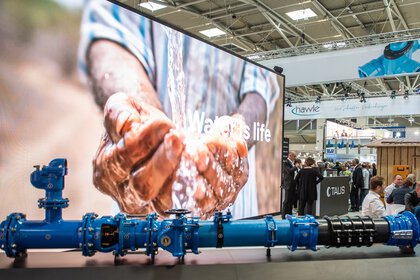 Representation of a water pipe system in front of a large display showing hands drawing water with the text “Water is life”.