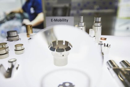 Mehrere Stanzformen und Zerstäuber liegen während der productronica zu Demonstrationszecken auf einem Tisch. Auf einem Schild steht „E-Mobility“.