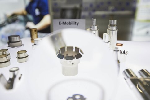 Various round metal parts on display in a brightly lit showcase at productronica. A sign reads 