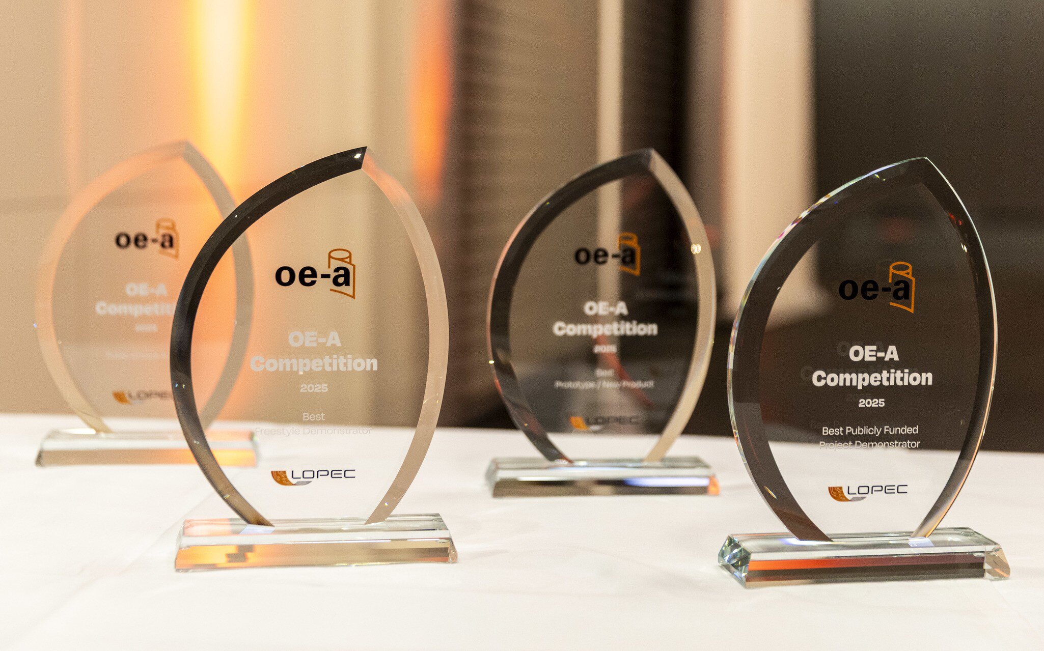 Four largely identical-looking glass trophies for different achievements in the “OE-A Competition” on a flat surface.