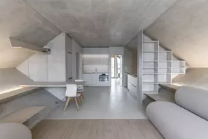 Minimalistisches Loft-Interieur mit geometrischen Wänden, schlichten Möbeln und einer kompakten Küche. Neutrale Töne dominieren den Raum.