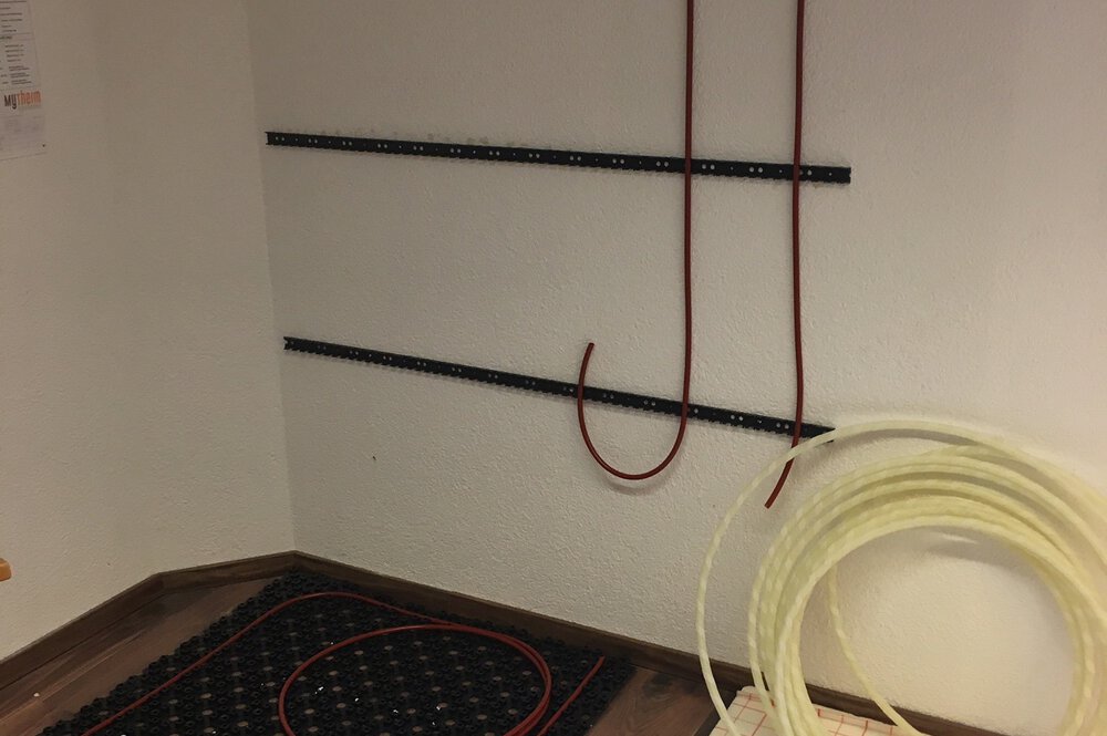 Wandecke mit Halteschienen für Schläuche und zwei aufgerollten Schläuchen auf dem Boden davor.