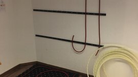 Wandecke mit Halteschienen für Schläuche und zwei aufgerollten Schläuchen auf dem Boden davor.