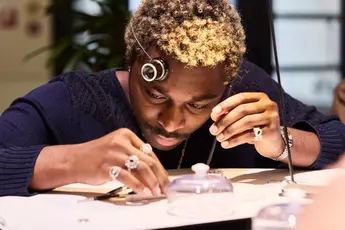 Person examining small objects with a magnifying eyepiece, concentrated and seated at a table.