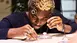 Person examining small objects with a magnifying eyepiece, concentrated and seated at a table.