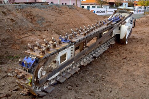 Große Grabenfräse mit rotierender Schneidkette auf einer Baustelle.