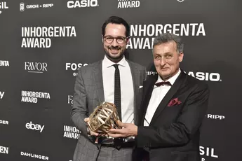 Zwei Männer lächeln und halten stolz die Trophäe in der Kategorie „Gemstone Design of the Year“ vor einer Logowand auf der AWARD-Gala.