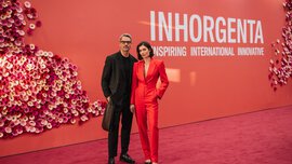 Ein Mann und eine Frau in Business-Kleidung stehen auf dem roten Teppich der INHORGENTA vor einer roten Wand mit Blumendokoration.