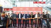 Eine Gruppe von Menschen steht auf einer Bühne bei einer Eröffnungsfeier einer Messe und schaut in die Kamera. Alle halten das Eröffnungsband in der Hand, dass zerschnitten werden soll.