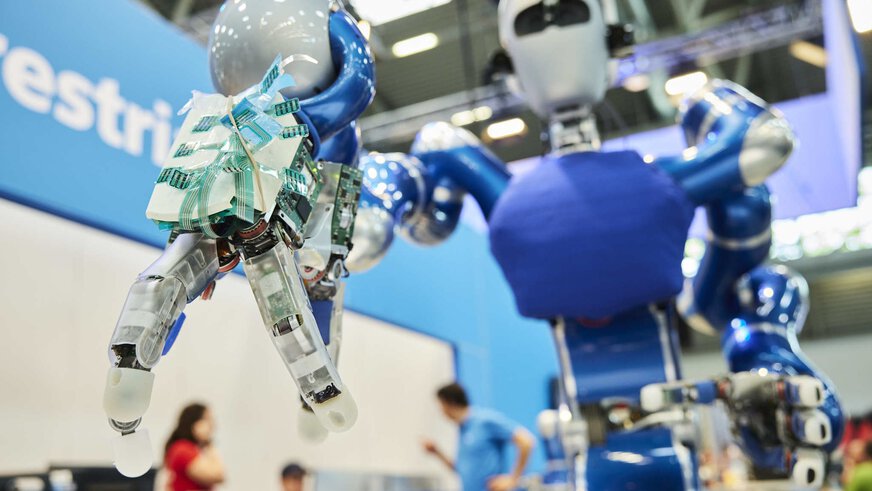 Close-up of the outstretched gripper arm of a humanoid robot on a trade fair stand.