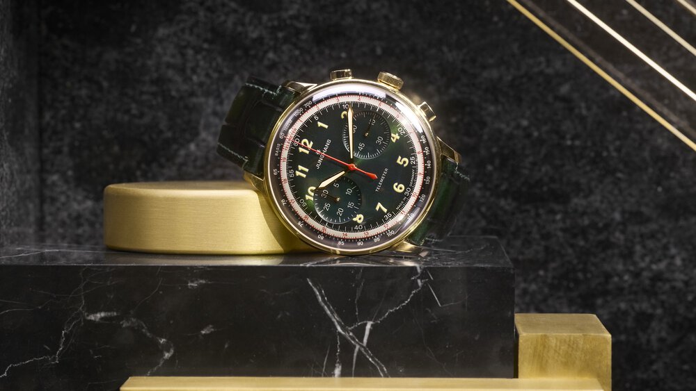 Golden watch with dark green dial and strap, on a black and gold marble surface.