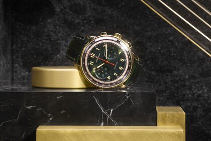 Golden watch with dark green dial and strap, on a black and gold marble surface.