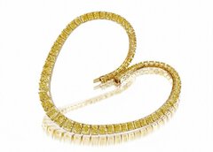 The Close-up view of a small delicate bracelet draped in a heart shape with several yellow stones on it.