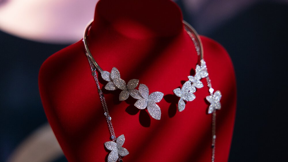 Eine Blumenkette mit Diamanten, präsentiert auf einer Schaufensterpuppe aus rotem Samt vor einem dunklen Hintergrund.