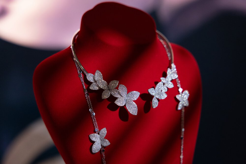 Eine Blumenkette mit Diamanten, präsentiert auf einer Schaufensterpuppe aus rotem Samt vor einem dunklen Hintergrund.