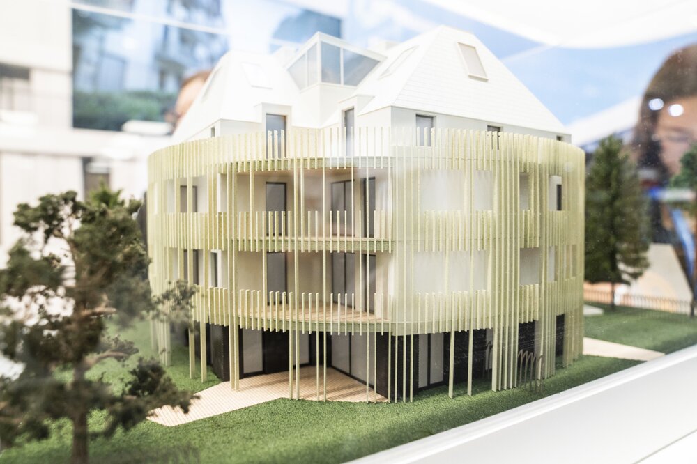 Ein modernes Architekturmodell eines mehrstöckigen Gebäudes mit einer vertikalen Lamellenfassade und grüner Landschaftsgestaltung.