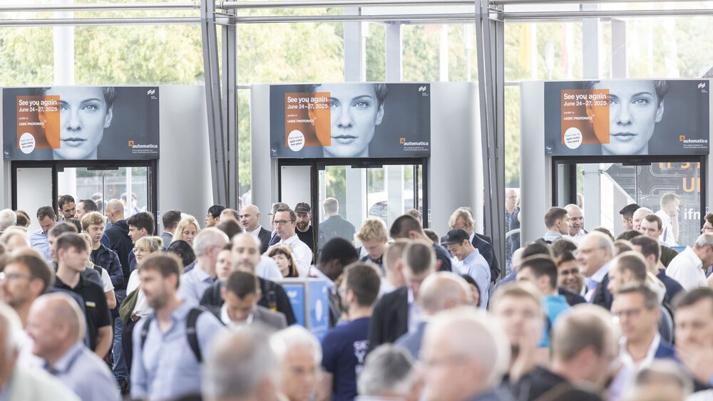 Eine große Menschenmenge bei der automatica 2023 in einem geschlossenen Raum mit sichtbaren Bannern im Hintergrund, die auf die automatica 2025 hinweisen.